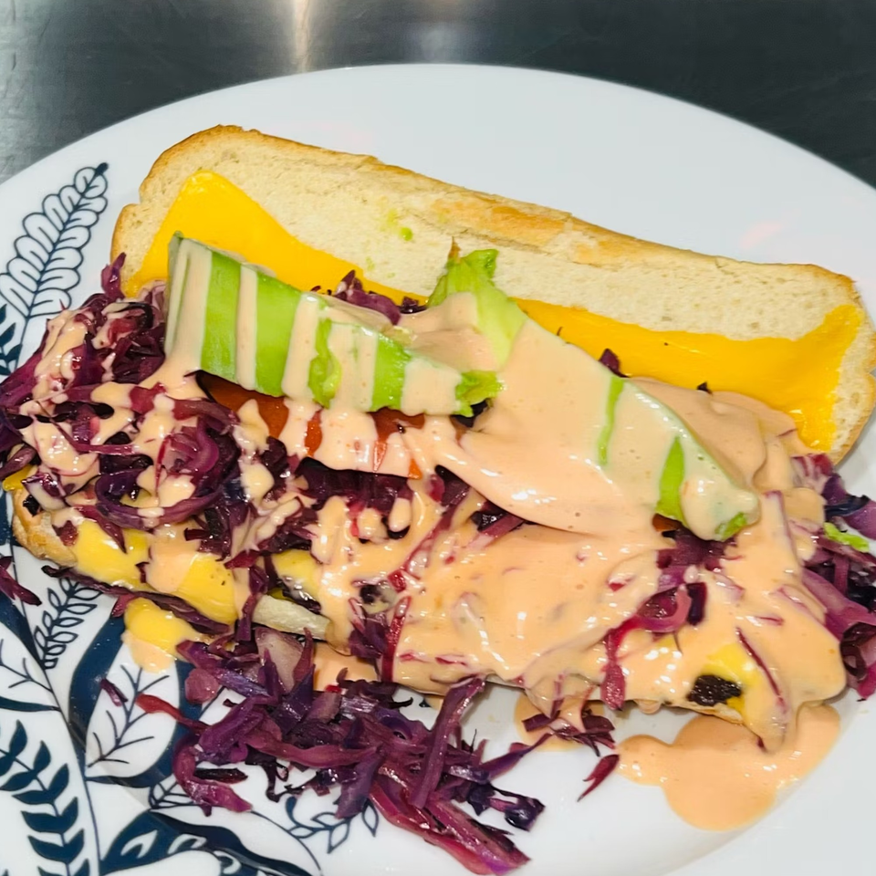 A Caribbean sandwich with cheese, red cabbage, avocado, and a creamy sauce on a white plate.