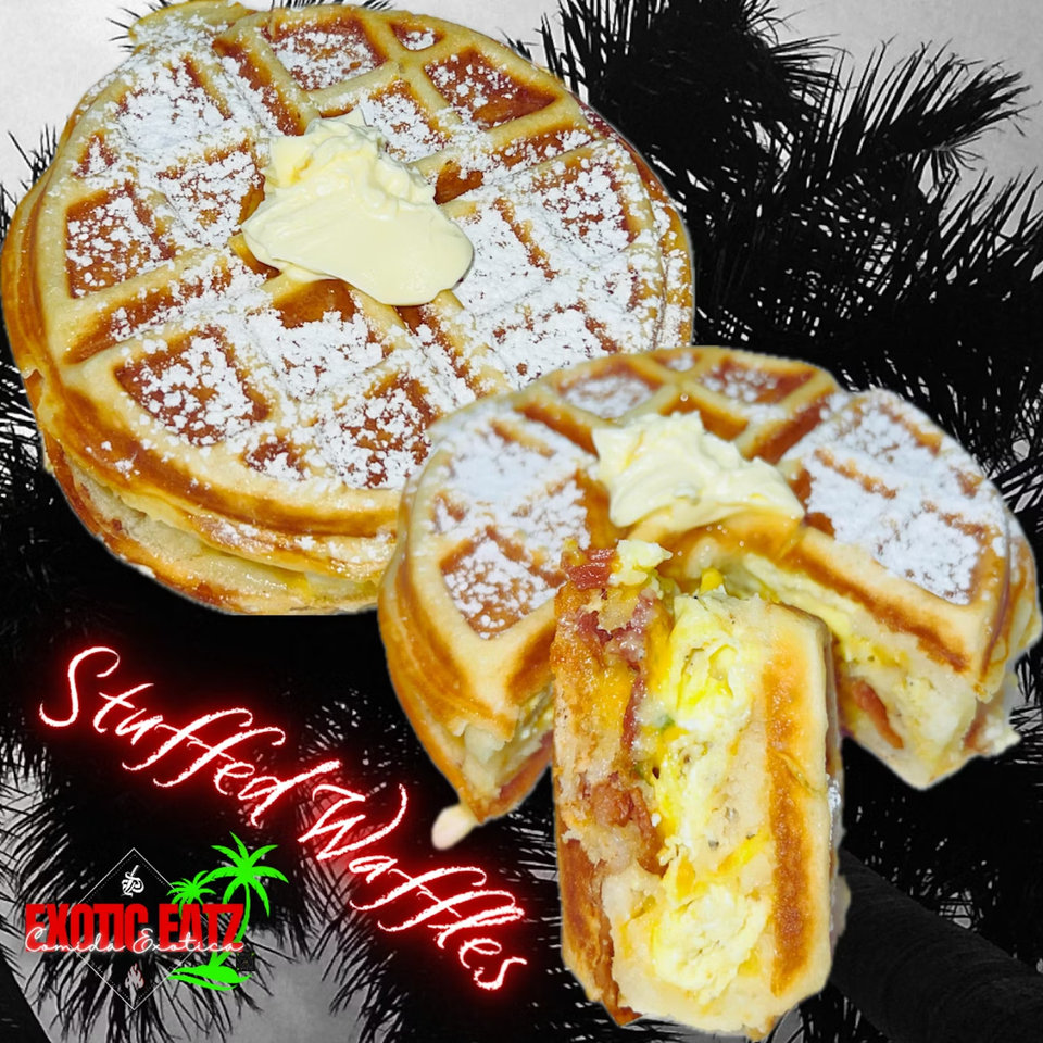 Two golden-brown stuffed waffles, dusted with powdered sugar and topped with butter, against palm fronds.