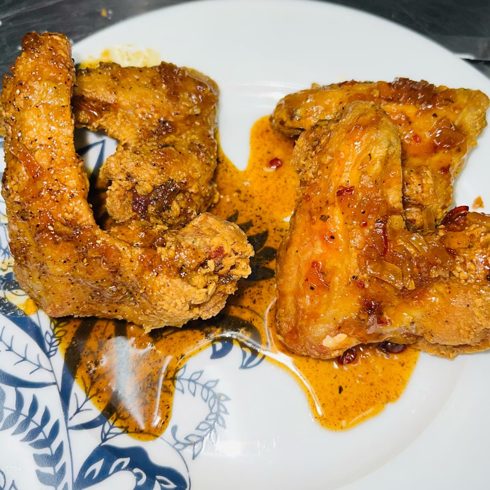 Two golden-brown Caribbean chicken wings, glistening with a spicy orange sauce, on a white plate.