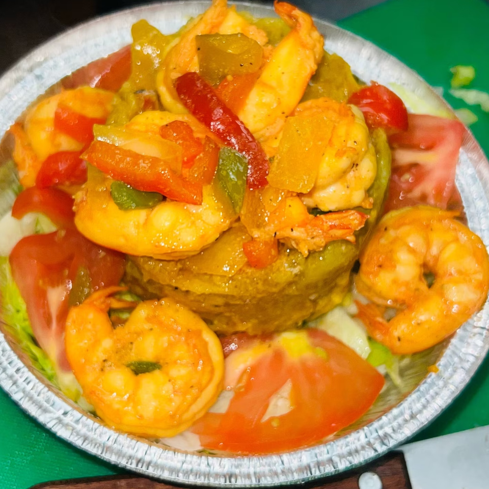 Caribbean shrimp dish with bell peppers, tomatoes, and lettuce in a foil container.